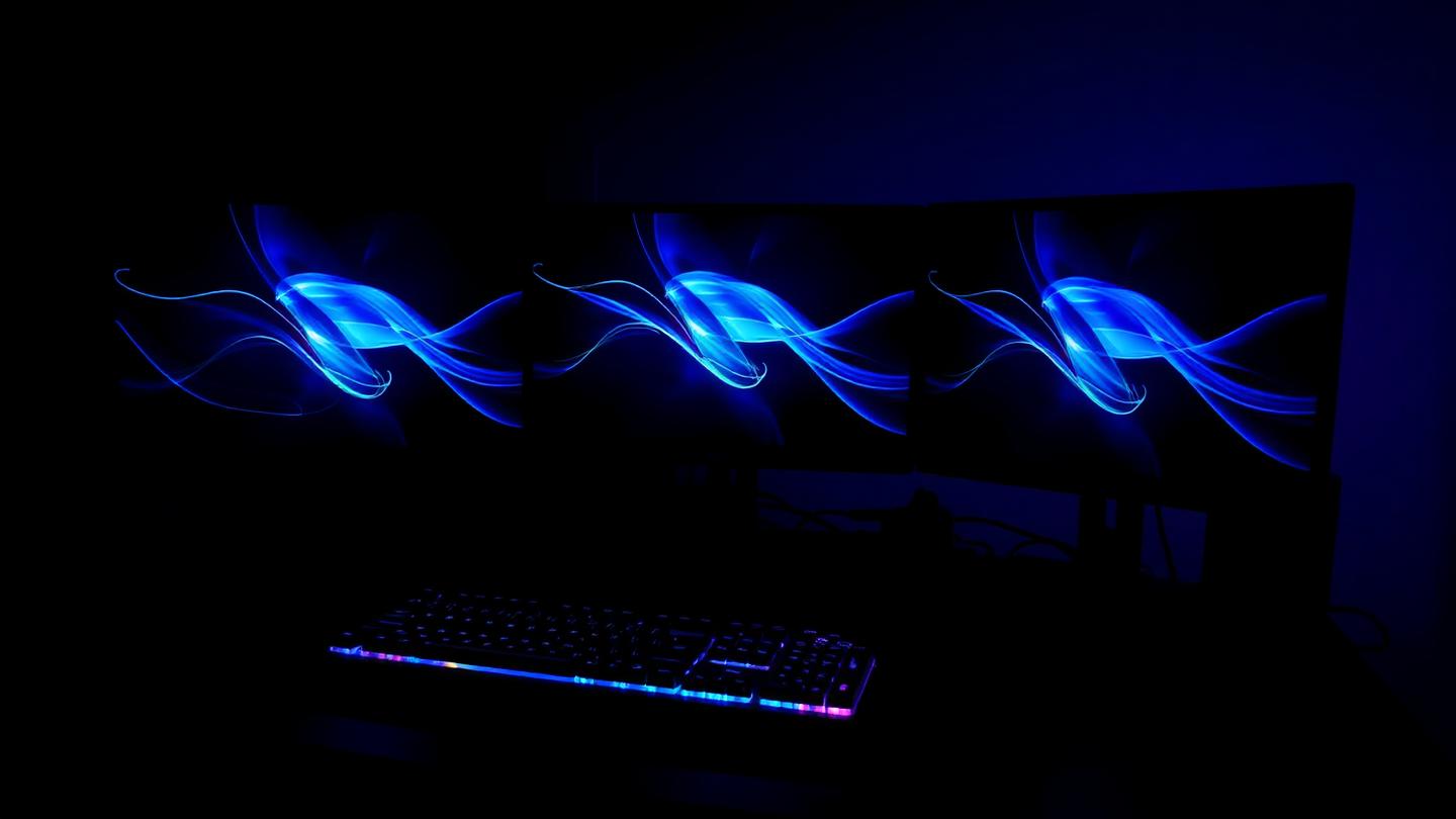 Triple écran courbé d'un setup esport diffusant une lumière bleutée dans l'obscurité.