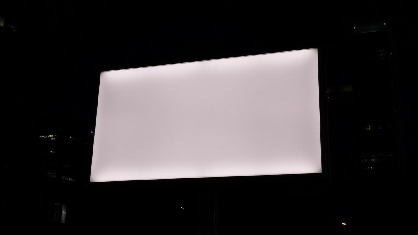 Panneau publicitaire urbain rétroéclairé dans la nuit, surface vierge sur fond de gratte-ciel.