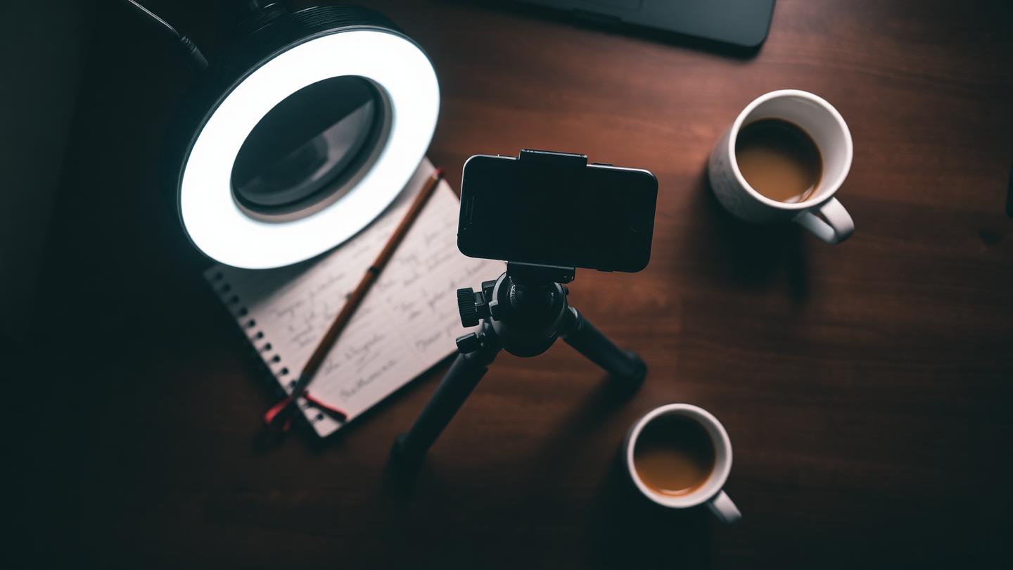 Espace de tournage minimaliste d'un créateur de contenu : smartphone sur trépied, ring light et carnet de notes.